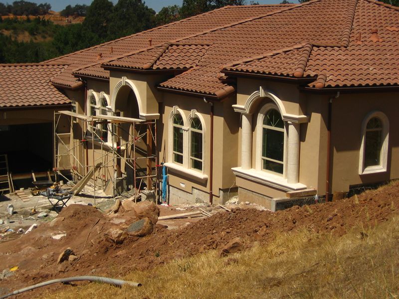 Stucco and clay tile roof being installed on a house under construction