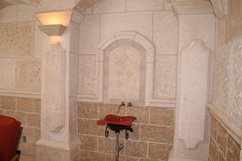 Limestone bathroom wall with carved arch detailing and a console basin