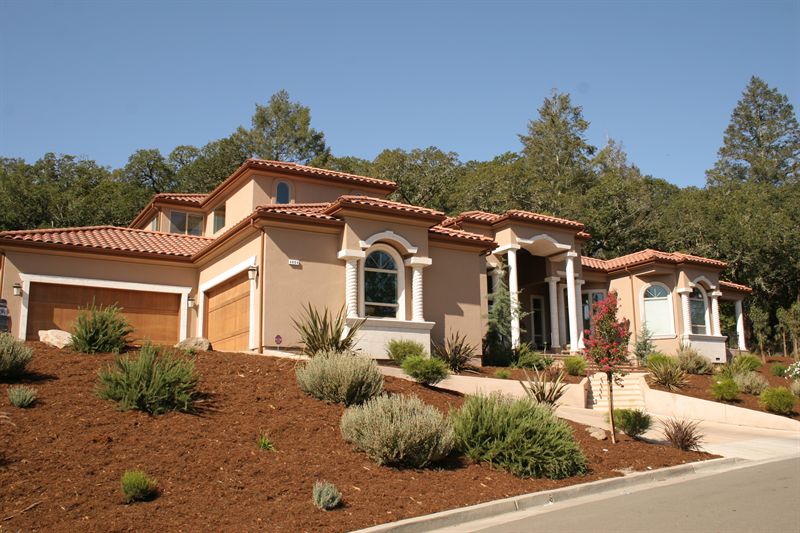 Mediterranean-style home with clay tile roof on a wooded lot