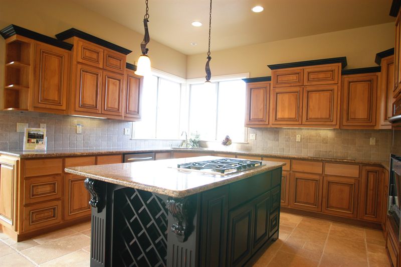 Kitchen with a green painted island, wood cabinetry and a tiled backsplash