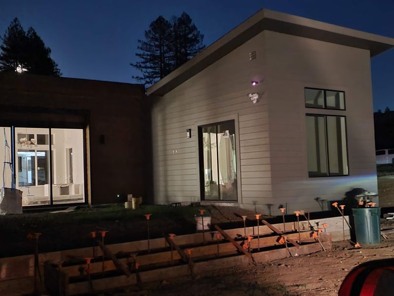 Modern home at dusk with lit windows and the hillside behind