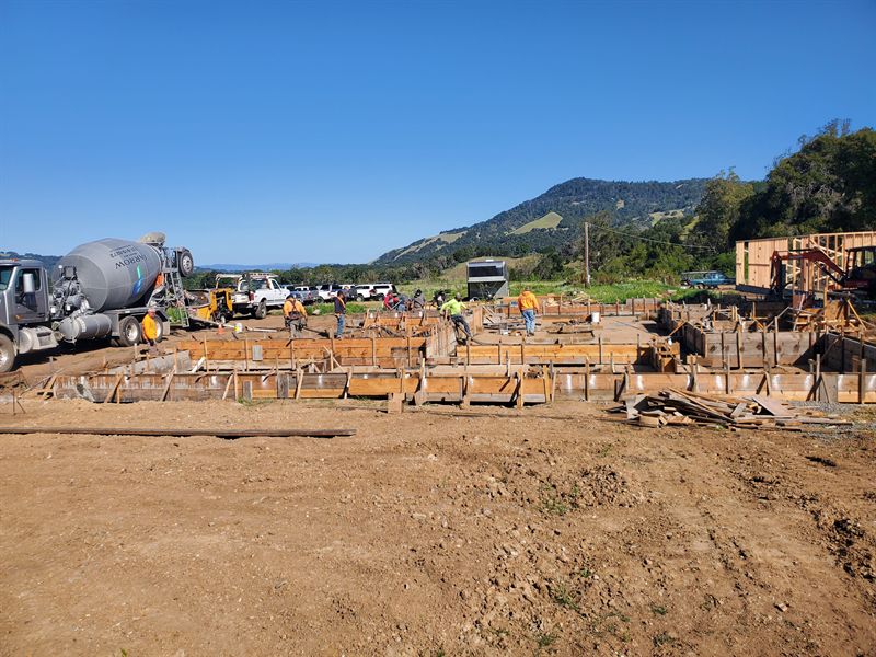 Foundation forms and rebar across a cleared lot with concrete trucks working