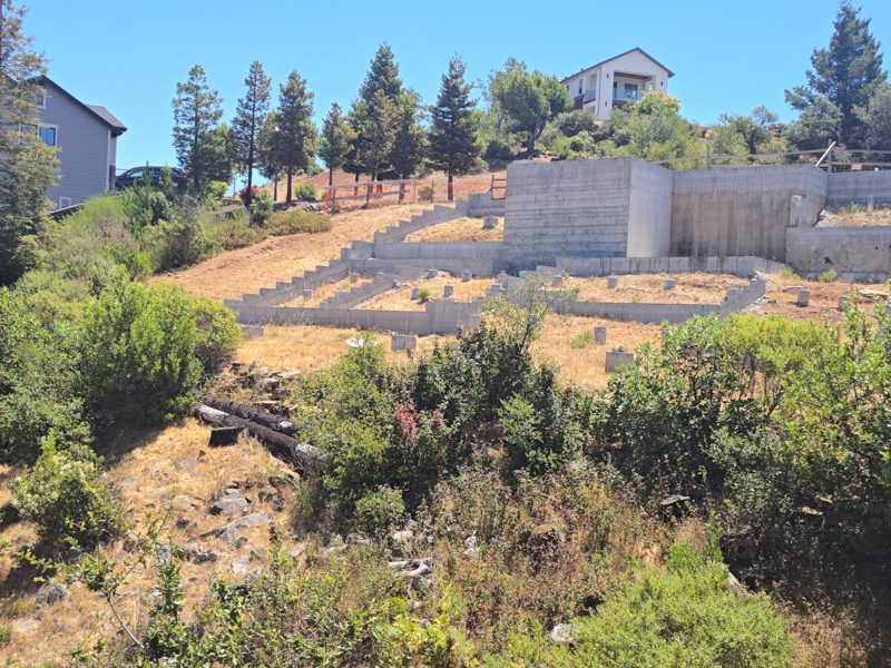 Hillside lot after the fire, with only the old concrete foundation and retaining wall left standing