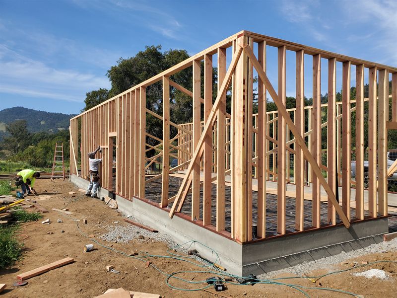 Workers raising a framed timber wall on a new concrete slab